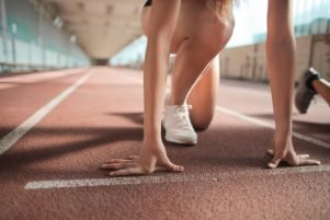 Focused female athlete in crouch start position preparing to sprint on an indoor track.