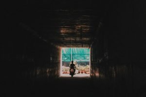 A dramatic silhouette of a person riding a motorcycle through a dark tunnel towards the light.